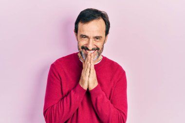 Orta yaşlı İspanyol bir adam gündelik giysiler içinde ellerini birleştirip af diliyor kendinden emin bir şekilde gülümsüyor.. 