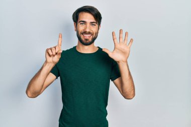 Gündelik beyaz tişört giyen genç İspanyol adam altı numarayı gösterip işaret ederken kendinden emin ve mutlu gülümsüyor.. 