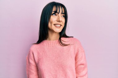 Kâküllü, kışlık süveter giyen genç esmer kadın yüzünde gülümsemeyle yan yana bakıyor, doğal bir ifade. Kendinden emin gülen. 