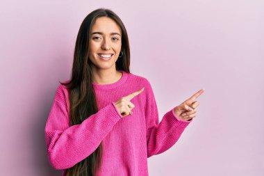 Yüzünde mutlu ve havalı bir gülümsemeyle parmaklarını yana doğru gösteren İspanyol genç bir kız. diş gösterme. 