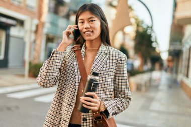 Genç Asyalı iş kadını şehirde akıllı telefon kullanarak mutlu bir şekilde gülümsüyor..