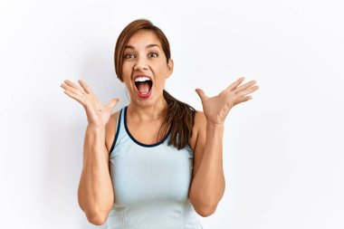 İzole edilmiş arka planda sportif kıyafetler giyen genç Latin bir kadın çılgın ve başarıyı kollarını kaldırıp heyecanla haykırarak kutluyor. Kazanan konsept 