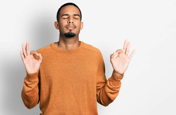 若いアフリカ系アメリカ人の男性がリラックスしたカジュアルな服を着て 目を閉じて指で瞑想ジェスチャーを行う笑顔 ヨガのコンセプト — ストック写真