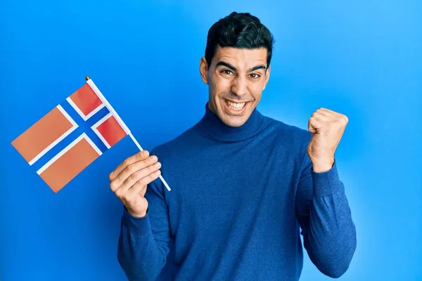 Hombre Hispano Guapo Sosteniendo Bandera Noruega Gritando Orgulloso Celebrando Victoria —  Fotos de Stock