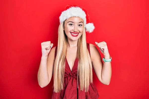 クリスマスの帽子をかぶっている若いブロンドの女の子は驚きを祝い 腕を上げて目を開けて成功したことに驚いています 勝者のコンセプト — ストック写真
