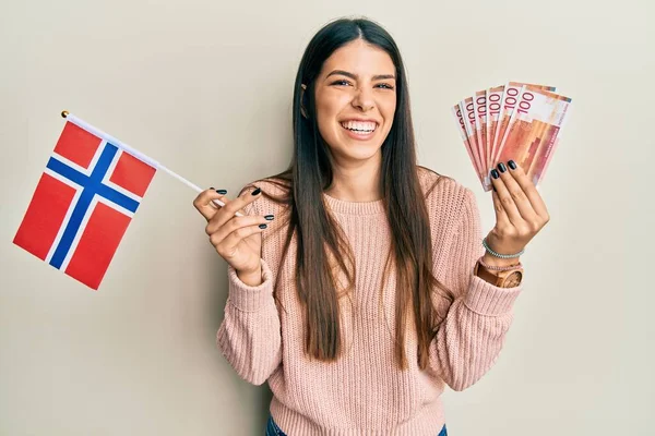 年轻的惊慌失措的女人举着诺威的国旗和克朗钞票 笑着大声笑着 因为有一个可笑的疯狂笑话 — 图库照片