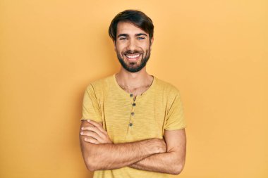 Gündelik kıyafetler giyen, kollarını kavuşturup kameraya gülümseyen genç İspanyol adam. pozitif kişi. 