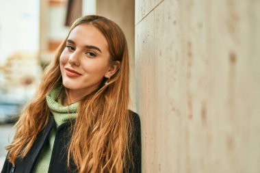 Genç sarışın kız gülümsüyor, mutlu bir şekilde şehirde duruyor..