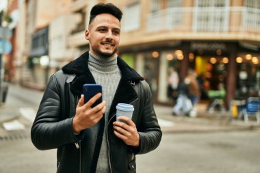 Genç Arap adam akıllı telefon kullanıyor ve şehirde kahve içiyor..