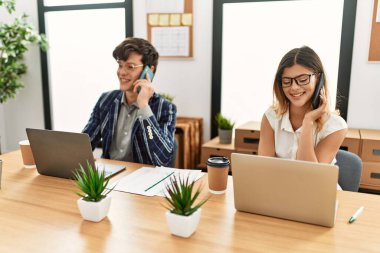 Ofiste akıllı telefon ve dizüstü bilgisayarla çalışırken gülümseyen iki iş adamı..