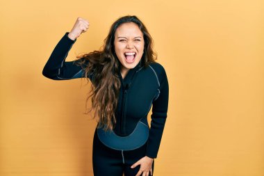 Genç İspanyol kız neoprene üniforması giyiyor kızgın ve kızgın yumruk kaldırıyor öfkeyle bağırırken. öfke ve agresif konsept. 