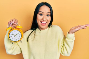 Güzel İspanyol bir kadın burun piercingli, çalar saat tutan mutlu bir gülümsemeyle başarıyı kutlayan ve elini kaldırmış bir ifadeyle kazanan bir kadın. 