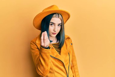 Sarı şapkalı, deri ceketli, İtalyan jestleri yapan genç ve modern bir kız. 