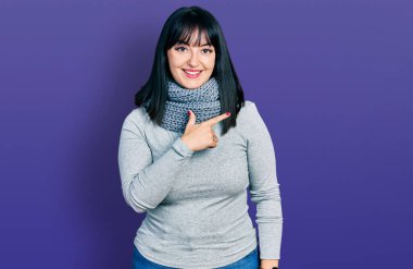 Genç İspanyol asıllı, uzun boylu, kış eşarbı takan neşeli, yüzünde gülümsemesi olan mutlu ve doğal bir ifadeyle el ve parmak uçlarını gösteren bir kadın. 