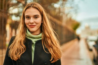 Genç sarışın kız gülümsüyor, mutlu bir şekilde şehirde duruyor..