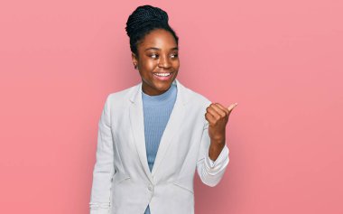 Genç Afro-Amerikan kadın, iş kıyafetleri içinde mutlu yüzle gülümseyen ve başparmağıyla yüzünü gösteren.. 