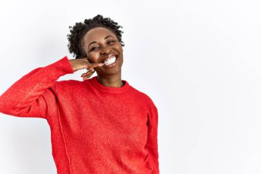 Genç Afrikalı Amerikalı kadın, izole edilmiş arka planda günlük giysiler giyip telefonla konuşurken gülümseyerek el ve parmaklarıyla telefon hareketi yapıyor. iletişim kavramları. 