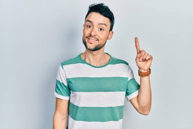 Gündelik kıyafetler giyen genç İspanyol bir numarayı gösterip işaret ederken kendinden emin ve mutlu bir şekilde gülümsüyor.. 