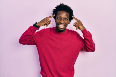 Gündelik giysiler giymiş genç Afro-Amerikan bir adam iki eliyle başını gösteren gülümseme, harika bir fikir ya da düşünce, iyi bir hafıza 