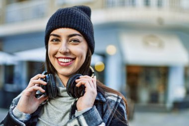 Genç İspanyol kadın şehirde kulaklık takarak mutlu gülümsüyor..