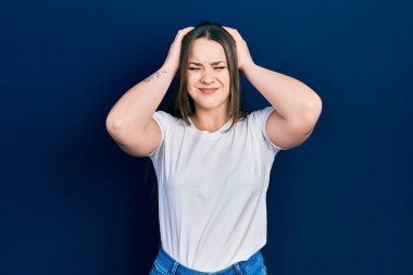 Beyaz günlük tişört giyen genç İspanyol kız baş ağrısı ve acı yüzünden çaresiz ve stresli çünkü migren. Eller başının üstünde.. 