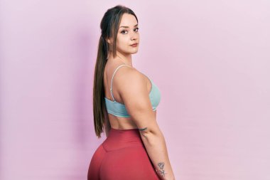 Vücut geliştiren genç bir kadın kaslarını gösteriyor. Spor kıyafeti giyiyor.