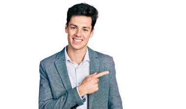 Genç İspanyol bir adam iş kıyafetleri içinde neşeli, yüzünde bir gülümseme, mutlu ve doğal bir ifadeyle elini ve parmağını kaldırıyor. 