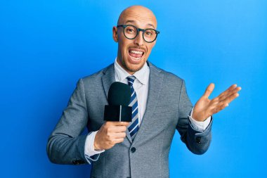 Kel adam, elinde sakallı mikrofonla başarıyı kutluyor. Gülümsüyor ve kazanan el kaldırıyor. 