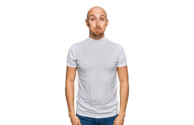 Sakallı, sıradan beyaz tişörtlü, komik suratlı kel bir adam. Havayla şişmiş ağız, çılgın bir ifade.. 