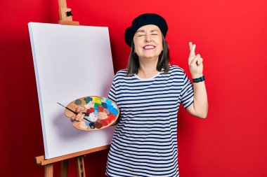 Orta yaşlı İspanyol kadın resim sehpası ile resim çiziyor umut ve gözler kapalı gülümseyerek el sallıyor. Şans ve batıl inançlar. 