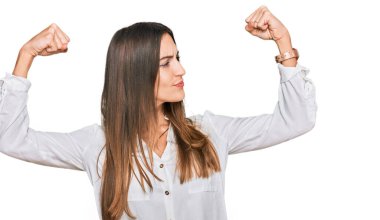 Genç ve güzel bir kadın sıradan kıyafetler giyip gururla gülümseyen kol kaslarını gösteriyor. fitness konsepti. 