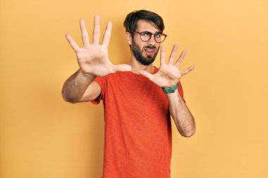 Günlük kıyafetler ve gözlük takan genç İspanyol adam korku ifadesinden korkmuş ve dehşete düşmüş. El kol hareketi yapmayı kes, şok içinde bağır. panik konsepti. 