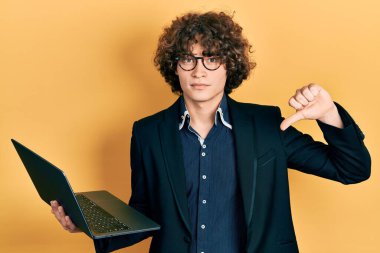 Kızgın suratlı, bilgisayar bilgisayarı kullanan yakışıklı bir genç. Eksi işareti, baş parmakları aşağıda, reddedilme konsepti. 