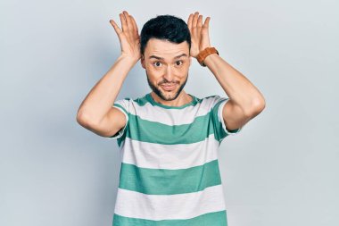 Gündelik kıyafetler giyen, tavşan kulağı yapan, avuçlarıyla alaycı ve şüpheci görünen genç İspanyol bir adam. Paskalya tavşanı konsepti. 