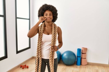 Spor salonunda afro saçlı, savaş halatları ve dudakları parmakları fermuar gibi kapalı genç Afrikalı Amerikalı bir kadın. gizli ve sessiz, tabu konuşması 