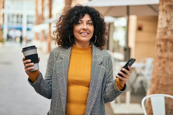 Genç İspanyol iş kadını akıllı telefon kullanıyor. Şehirde kahve içiyor..