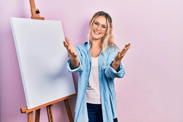 Hermosa Joven Rubia Parada Junto Caballete Pintor Blanco Mirando Cámara — Foto de Stock