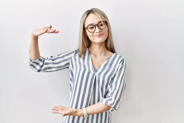 亚洲年轻女子身穿休闲装 戴着眼镜 手举着大号和大号的手势 测量符号 微笑着看着摄像机 计量概念 — 图库照片