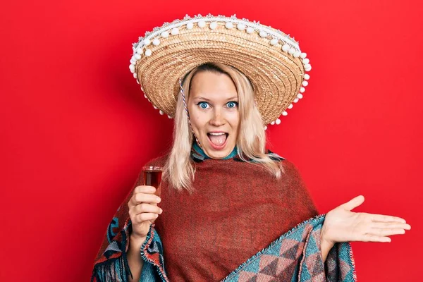 美しいですCaucasianブロンド女性身に着けているお祝いメキシカンPoncho飲料Tequilaショット祝い達成を祝います幸せな笑顔と勝者式とともに上げ手 — ストック写真