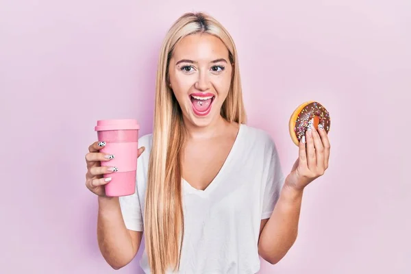 年轻的金发女郎吃着甜甜圈 喝咖啡庆祝着疯狂的成功 睁开眼睛尖叫着兴奋地惊叹着 — 图库照片