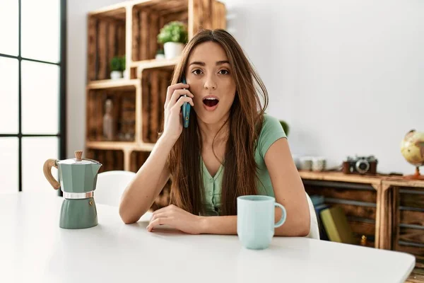 Jonge Spaanse Vrouw Praten Smartphone Zitten Tafel Thuis Bang Verbaasd — Stockfoto