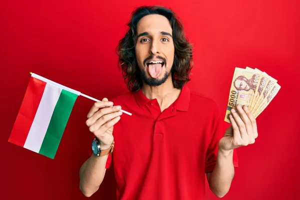 Joven Hombre Hispano Sosteniendo Bandera Húngara Forints Sacando Lengua Feliz —  Fotos de Stock