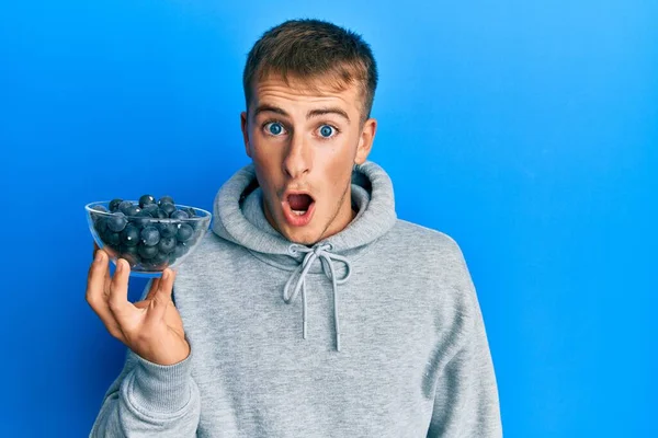 Young Caucasian Man Holding Bowl Blueberries Scared Amazed Open Mouth — Stock Photo, Image