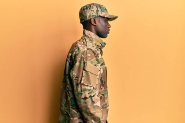 Asker üniforması giyen Afro-Amerikan genç adam, rahat bir görünüm ve kendine güvenen bir gülümseme takınıyor.. 