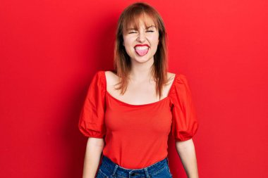 Kırmızı tişört giyen kızıl saçlı genç bir kadın komik bir ifadeyle dilini dışarı çıkartıyor. duygu kavramı. 