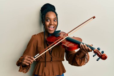 Saçları örgülü, keman çalan Afrikalı Amerikalı bir kadın çılgın bir şekilde keman çalıyor ve gözleri açık heyecanla haykırıyor.. 