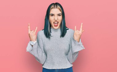 Genç, modern bir kız, gündelik kazak giyip çılgın bir ifadeyle bağırıyor ve elleri havada rock sembolü yapıyor. Müzik yıldızı. ağır kavram. 