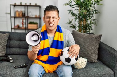 Genç İspanyol holigan adam futbol takımını destekliyor evdeki kanepede oturuyor..