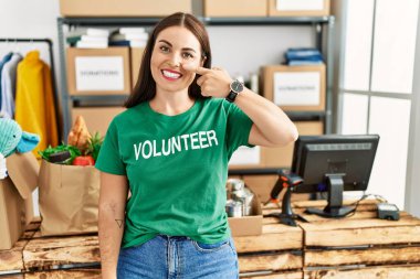Bağışta gönüllü tişört giyen genç esmer kadın el ve yüz yüze, neşeli bir şekilde gülümsüyor. güzellik konsepti 