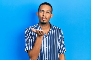 Gündelik giysiler giymiş genç Afro-Amerikan bir adam kameraya bakıp havada el ele öpüşerek sevimli ve seksi oluyor. aşk ifadesi. 